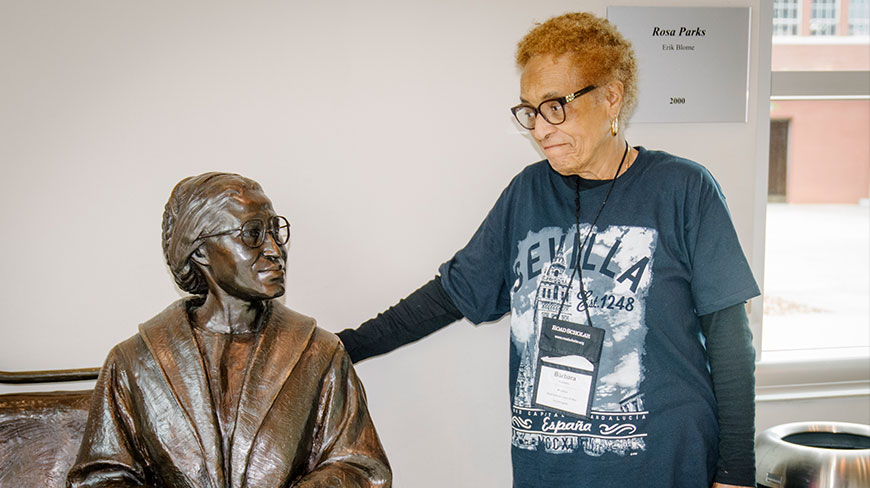 An older woman with glasses stands with her hand on the shoulder of a bronze statue of Rosa Parks at a museum in Montgomery.