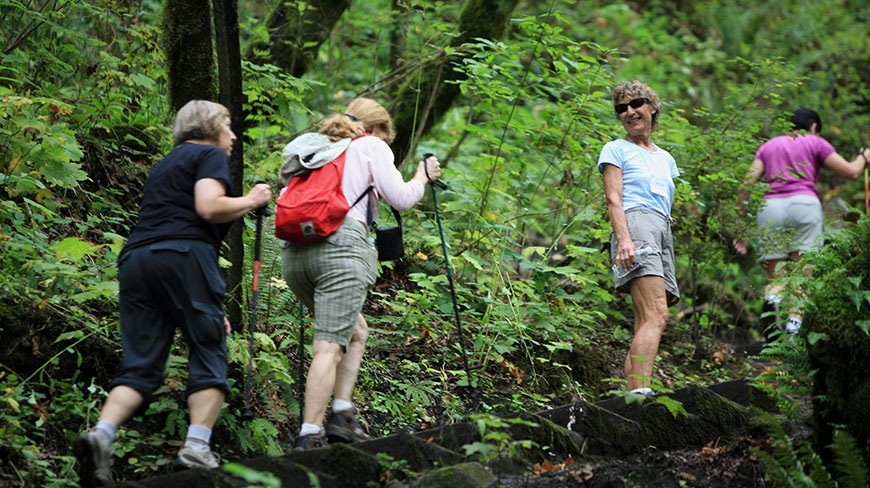 Four women enjoy a hike up a set of trail stairs in a lush, green forest in Oregon.