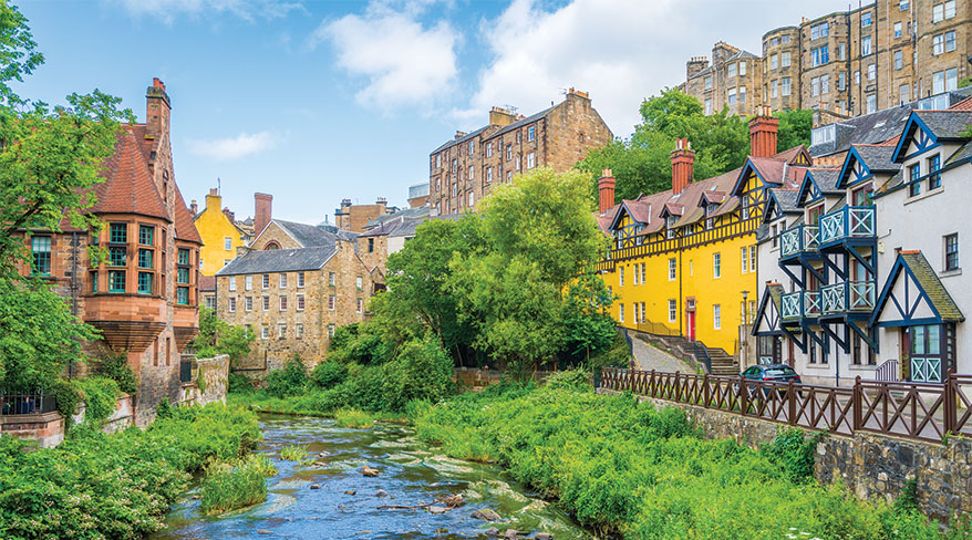 Colorful historic buildings of Dean Village in Edinburgh, Scotland, line the lush green banks of the Water of Leith river.