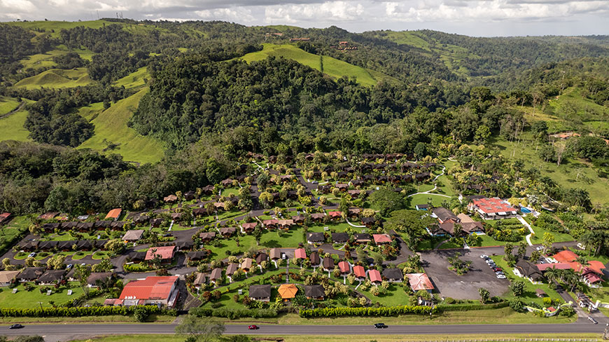 An aerial view shows a resort nestled among the lush, green, rolling hills of Costa Rica near a highway.
