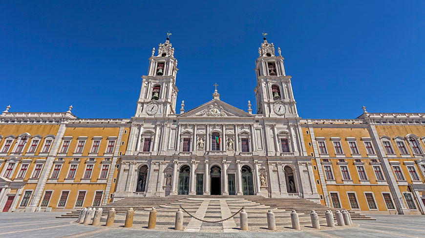 The grand facade of the Mafra National Palace in Portugal stands under a clear, bright blue sky.