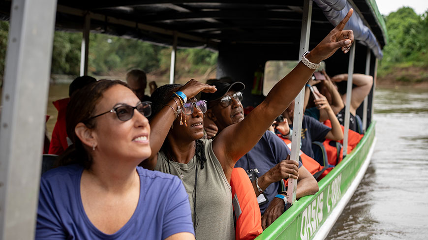 A group of travelers on a covered river boat in Costa Rica excitedly look and point at something in the distance.