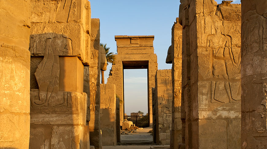 Golden light illuminates the massive stone pillars carved with hieroglyphs at the Karnak Temple in Egypt.