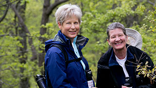 Two smiling women in hiking gear pause on the Appalachian Trail in Pennsylvania, surrounded by lush green forest foliage.
