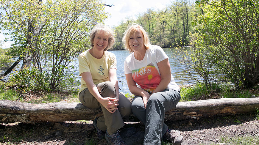 Two women sit on a log by a lake while hiking on the Appalachian Trail in Pennsylvania.