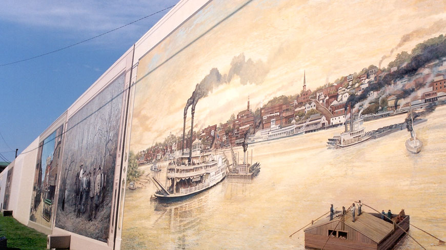 A large mural in Vicksburg, Mississippi, depicts 19th-century steamboats navigating the busy riverfront below the historic hillside town.