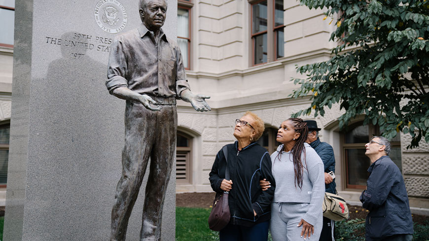 A small group of people on a tour in Atlanta looks up at the bronze statue of President Jimmy Carter at the Georgia Capitol.