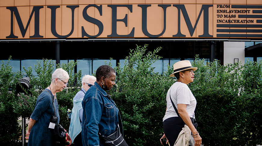 A group of visitors walks past the entrance to the Legacy Museum in Montgomery, Alabama, which reads "From Enslavement to Mass Incarceration."