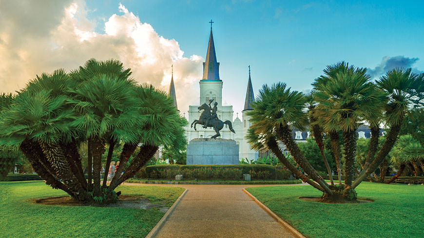 St. Louis Cathedral in New Orleans is viewed from a park with an equestrian statue and palm trees in the foreground.