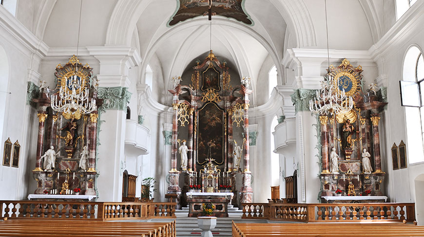 The ornate, vaulted interior of the Jesuit Catholic Church in Switzerland, showing the grand marble altars and wooden pews.