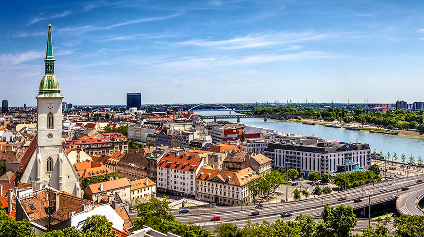 A panoramic view of Bratislava, Slovakia, on a sunny day, showcasing the historic old town and the Danube River.