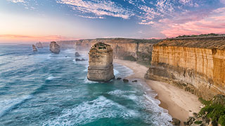 The Twelve Apostles sea stacks stand in the ocean off the coast of the Great Ocean Road in Victoria, Australia, under a colorful sky.