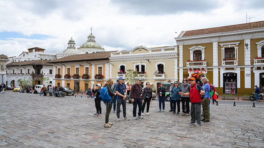 A group of travelers on a walking tour stand in the cobblestone plaza before the historic San Francisco Church and Convent in Quito, Ecuador.