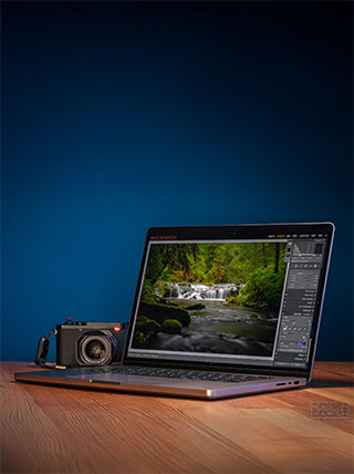 A laptop displaying a photo of a waterfall in Ecuador sits on a wooden desk next to a digital camera, illustrating a photography course.