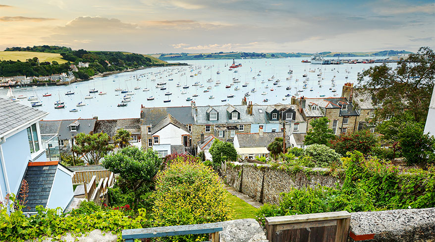 Houses and lush gardens overlook a harbor filled with sailboats in the coastal town of Falmouth, England.
