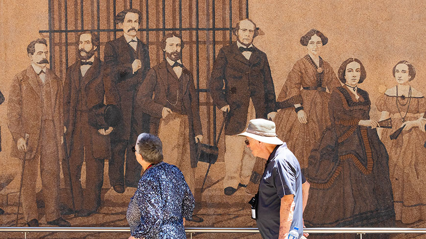 Two people look at a large historical mural depicting 19th-century figures on a street in Havana, Cuba.