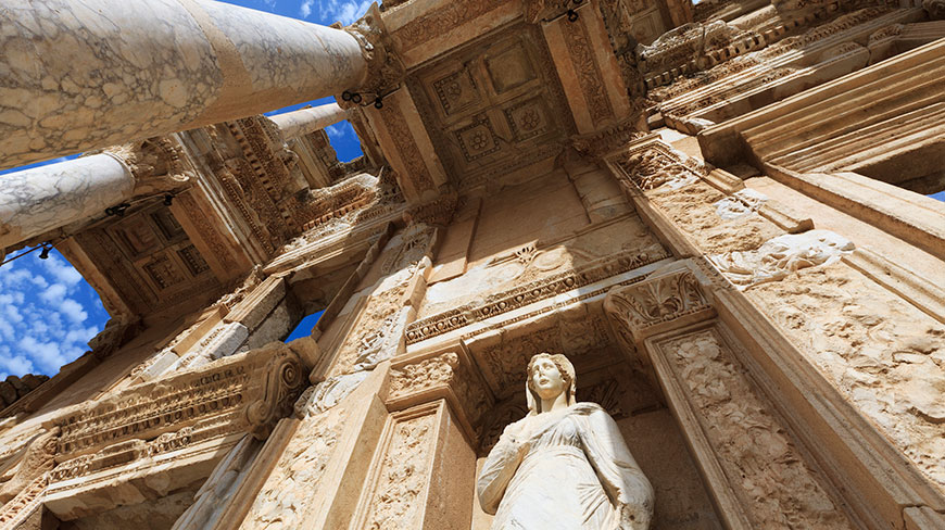 Looking up at the ornate facade of the ancient Library of Celsus in Ephesus, Turkey, against a bright blue sky.