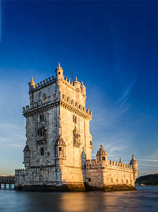 Lisbon's Belém Tower, a stone fortress in the water, is bathed in warm sunlight under a clear blue sky.