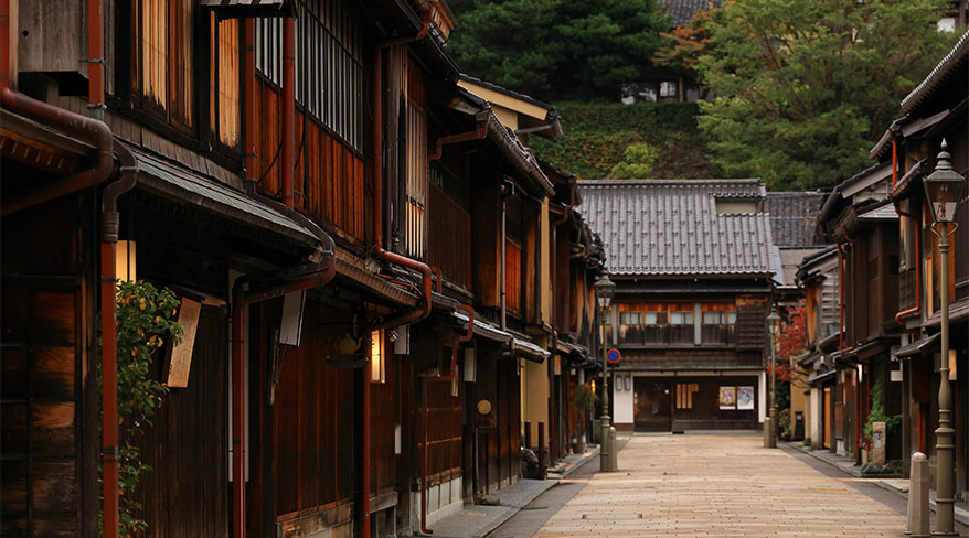 Traditional dark wood buildings line a quiet, empty stone-paved street in the Higashi Chaya District of Kanazawa, Japan.