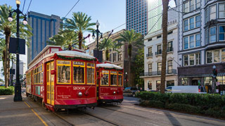 Two red streetcars on Canal Street in New Orleans, Louisiana, with palm trees and city buildings in the background.