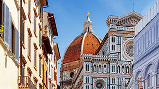 The ornate, marble facade and large dome of the Basilica di Santa Maria del Fiore in Florence, Italy, are seen from a nearby street.