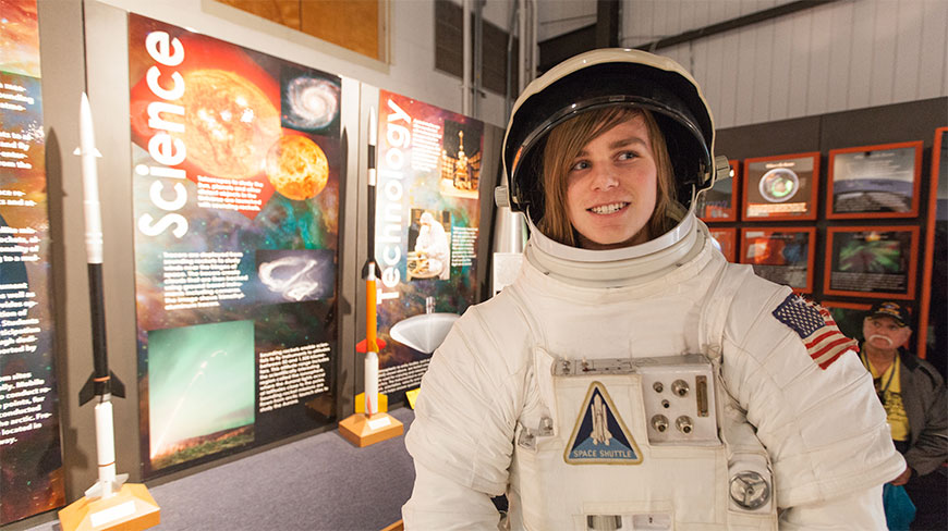A smiling young person wears an astronaut suit while visiting a NASA science and technology exhibit in Virginia.