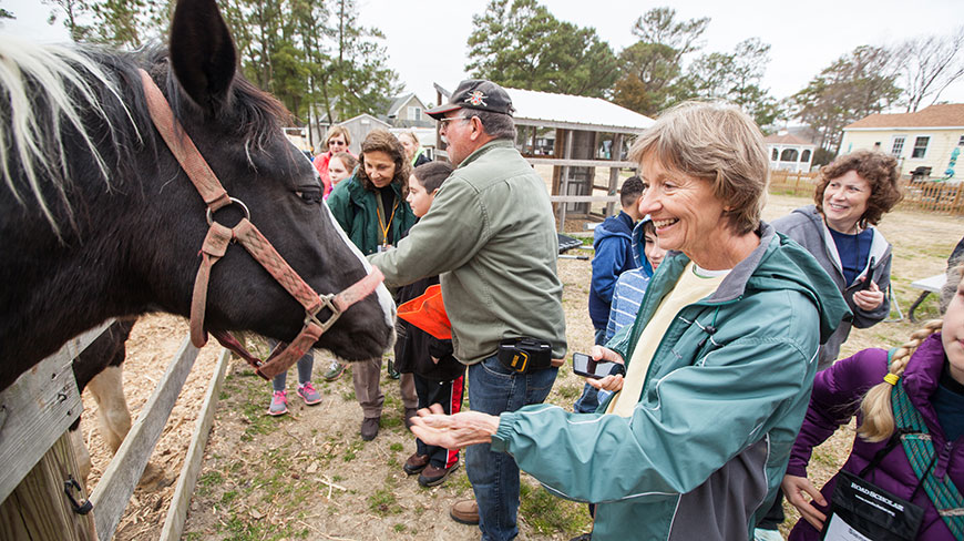 A group of adults and children gather around to pet a Chincoteague pony at a ranch in Virginia.