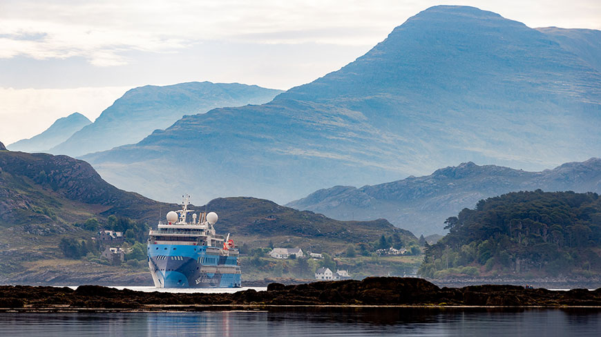 The Ocean Albatros expedition ship sails through Loch Torridon in Scotland, surrounded by misty mountains and a small village.