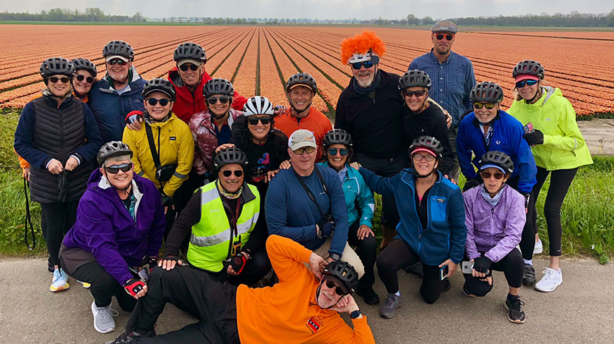 A group of cyclists in helmets poses for a photo in front of a large tulip field in the Netherlands.