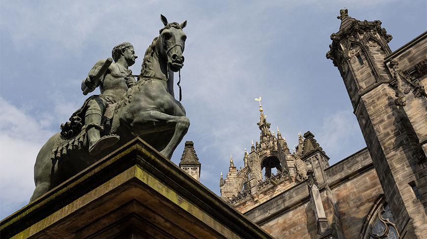 A low-angle view of the equestrian statue of Charles II of England beside the intricate stone spires of St Giles' Cathedral in Edinburgh, Scotland.