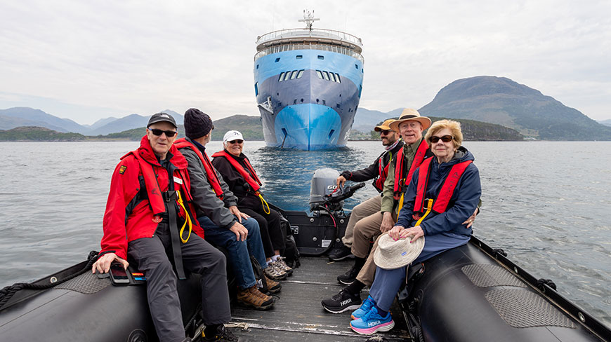 A group of travelers in a Zodiac boat approach their expedition ship on the waters of Loch Torridon in Scotland.