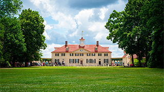 A wide view of the Mount Vernon presidential home in Virginia, with its iconic red roof and large front lawn framed by lush green trees.