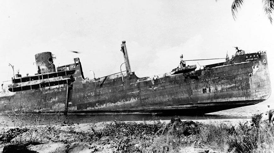 A black and white photograph of the Japanese transport ship Kinugawa Maru beached on a tropical shore.