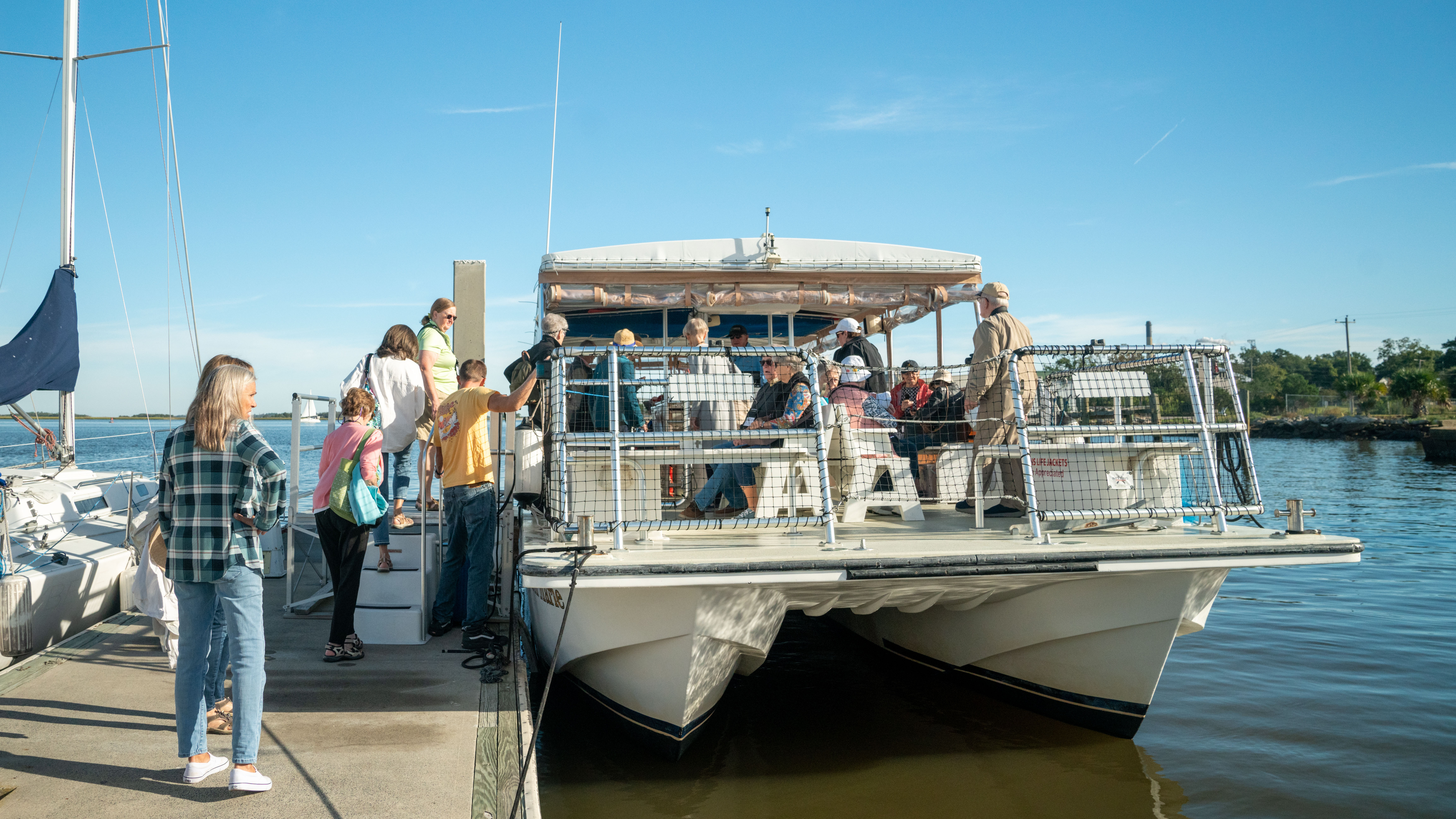 A group of travelers boards a white catamaran tour boat from a dock on a sunny day in Amelia Island, Florida.