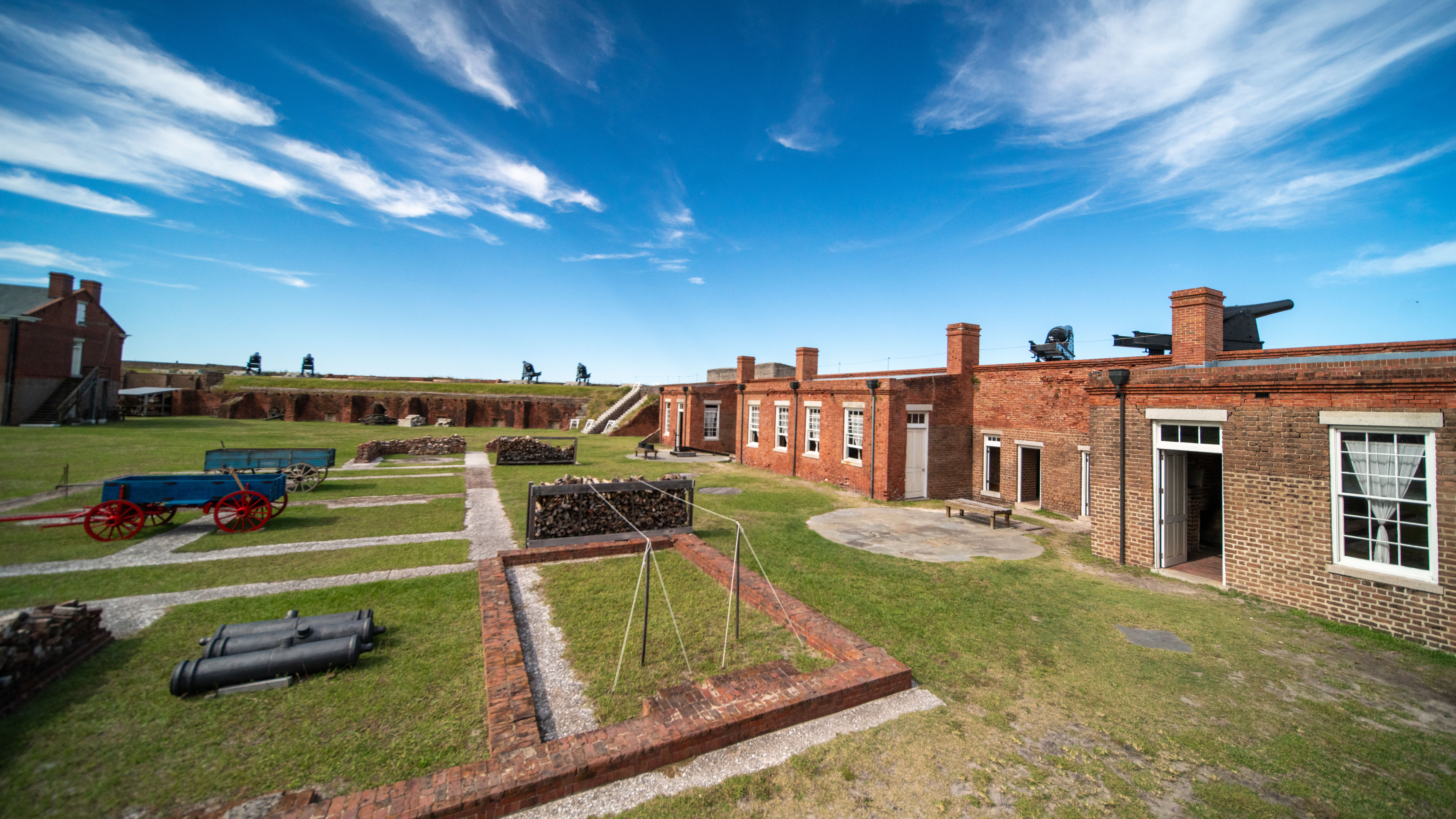 The red brick buildings and green grassy courtyard of Fort Clinch on Amelia Island, Florida, sit under a wide, blue, cloud-streaked sky.