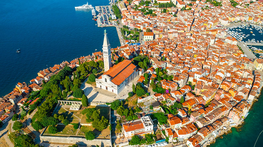 An aerial view of the Church of St. Euphemia and the old town of Rovinj, Croatia, on a peninsula surrounded by blue water.