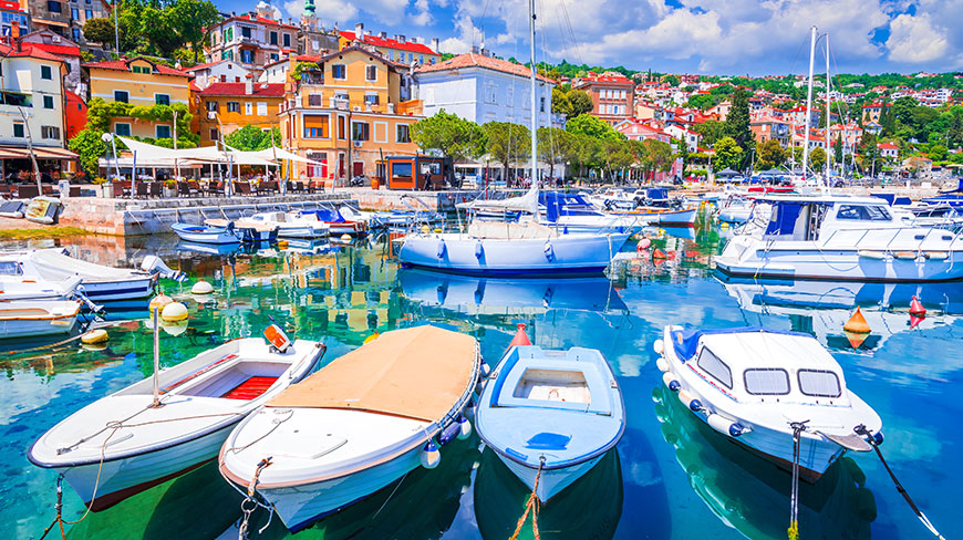 Colorful buildings line the hillside above a harbor full of boats on the Adriatic Sea in Opatija, Croatia.
