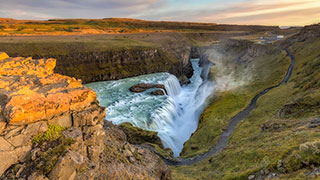 The powerful Gullfoss Falls cascades through a rugged canyon in Iceland during a golden sunset.