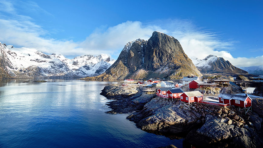 The scenic fishing village of Reine in the Lofoten Islands, Norway, with its iconic red cabins nestled between stunning fjords and snow-capped mountains.