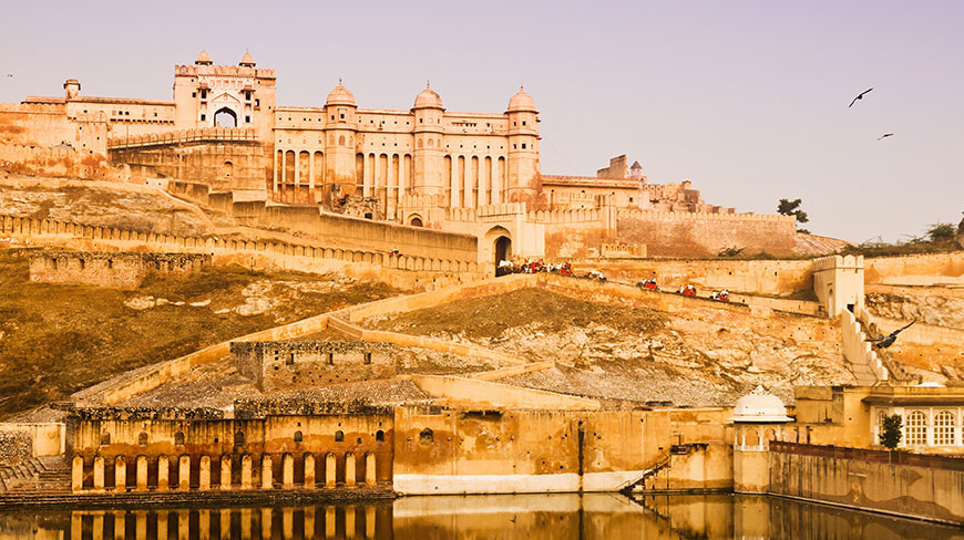 The sprawling Amber Fort in Jaipur, India, glows in the warm light of sunset as elephants ascend the path.