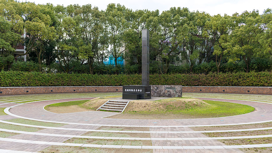 The black pillar of the Nagasaki Atomic Bomb Memorial stands in the center of a circular paved park in Japan.