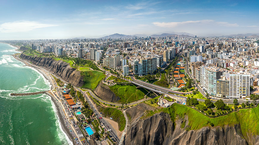 A panoramic aerial view of Lima, Peru's modern cityscape situated on green cliffs overlooking the Pacific Ocean coastline.