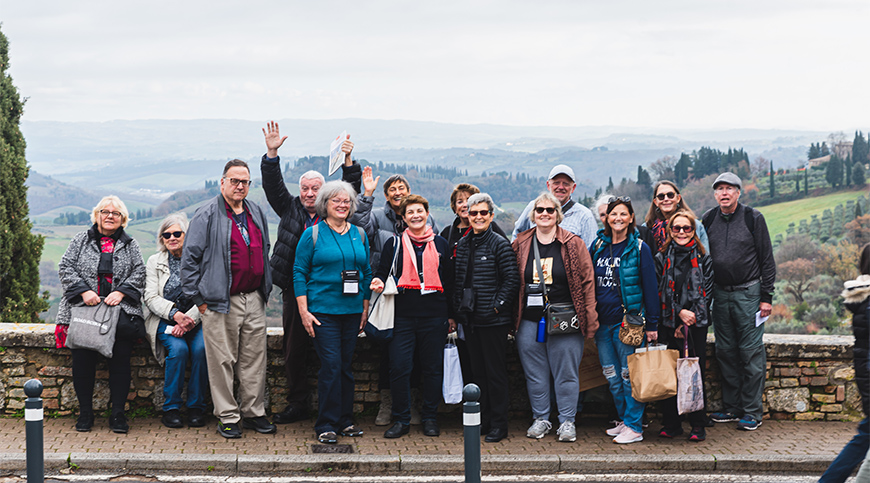 A group of travelers smiles for a photo in front of the rolling hills of the Italian countryside in Tuscany.