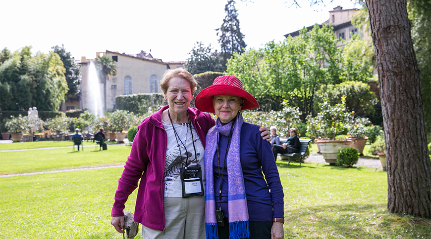 Two women on a tour smile together in a sunny garden in Italy.